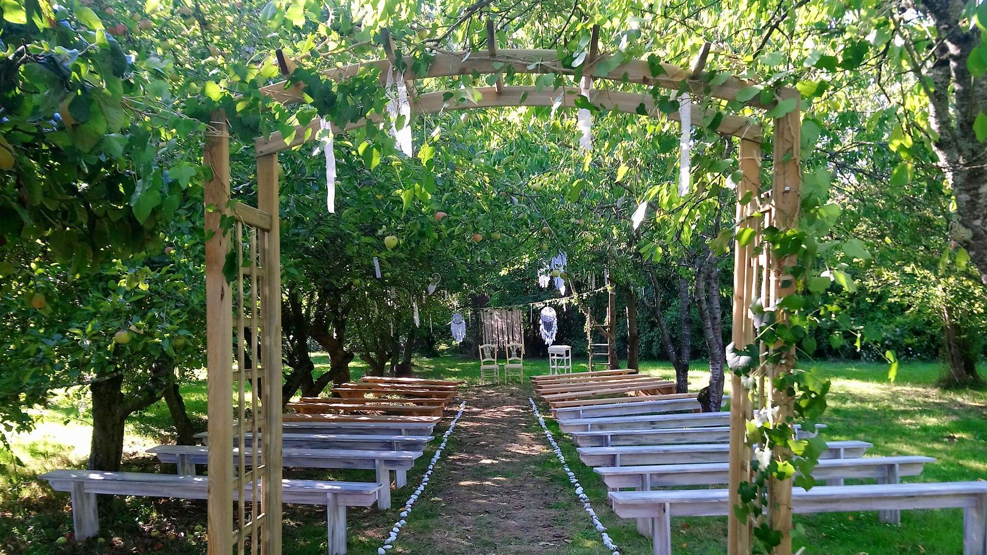 Allée de bancs sous l'arche de bois du verger, prête pour une cérémonie laïque